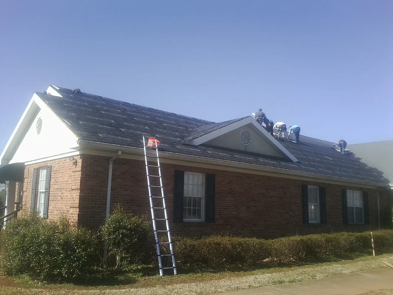 Crew tearing shingles off a brick ranch roof with a ladder set — Emergency Roof Repair work by our crew in Frisco