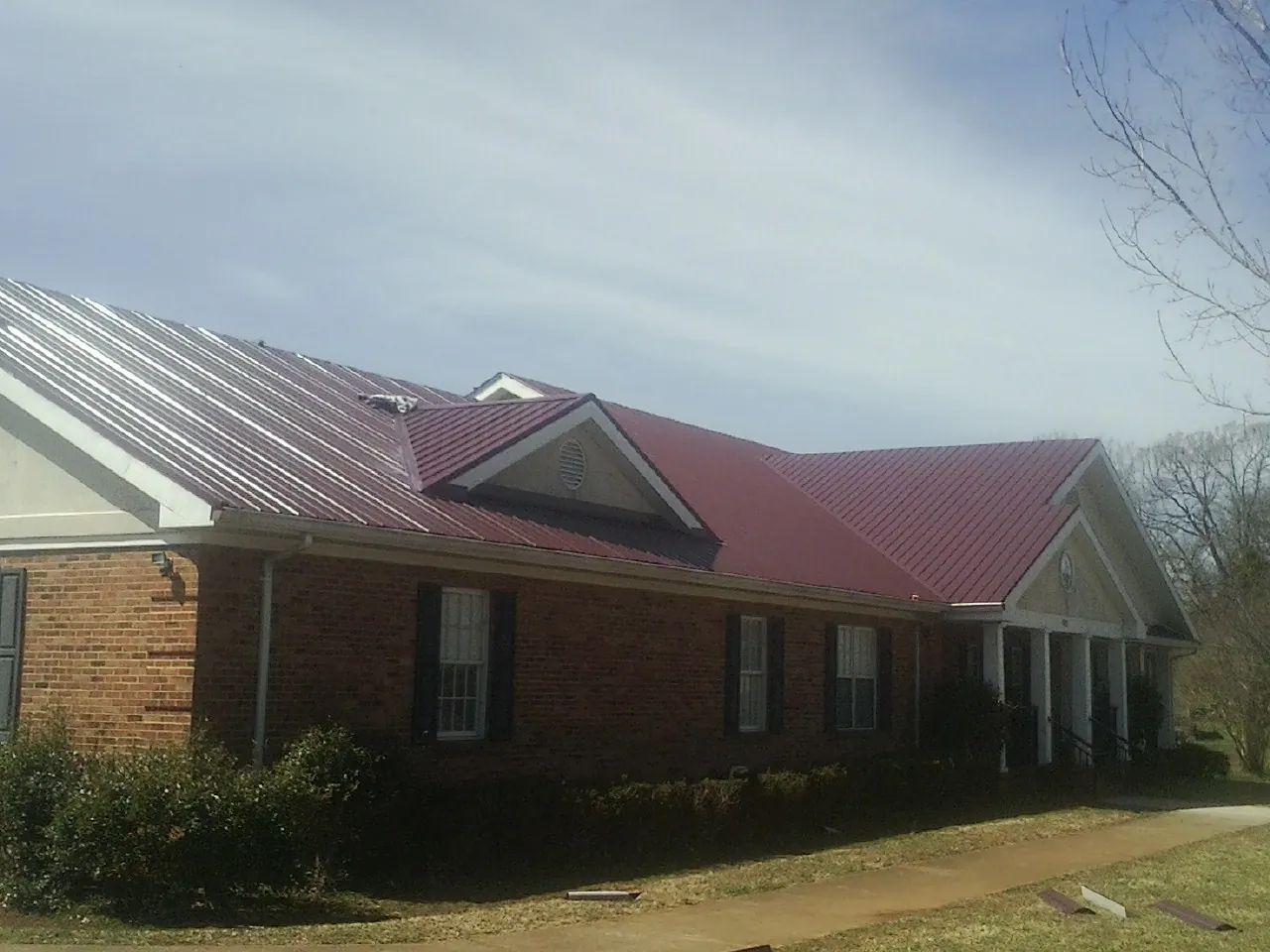Red metal roof with gabled entries on a long brick building, from a Hail Damage Roof Repair job in Frisco