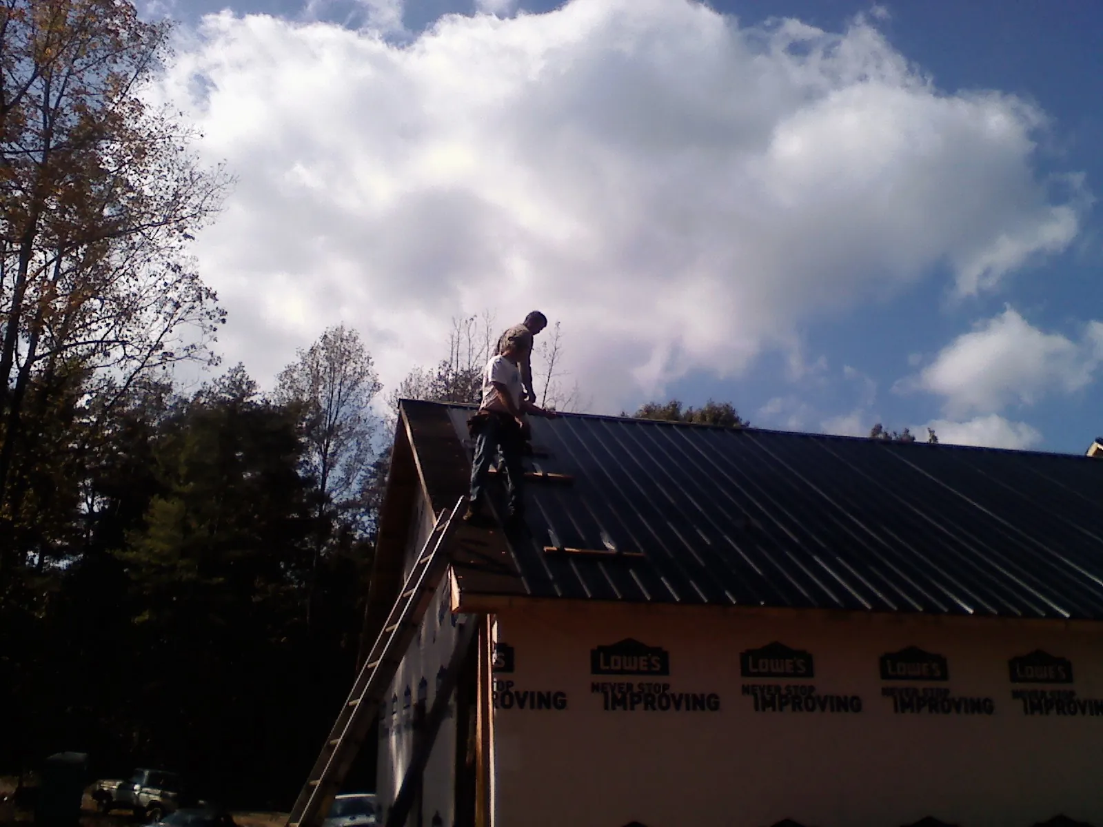 Roofer fastening dark metal panels high against a cloudy sky, from a Roof Inspection job in Frisco